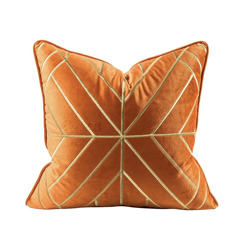 K&ouml;nnte beinhalten: Ein orangefarbenes Samtkissen mit einem geometrischen Muster aus goldenen Stickereien.