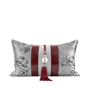 May include: A decorative pillow with a silver and red striped design. The pillow has a tassel and a round, white pendant.