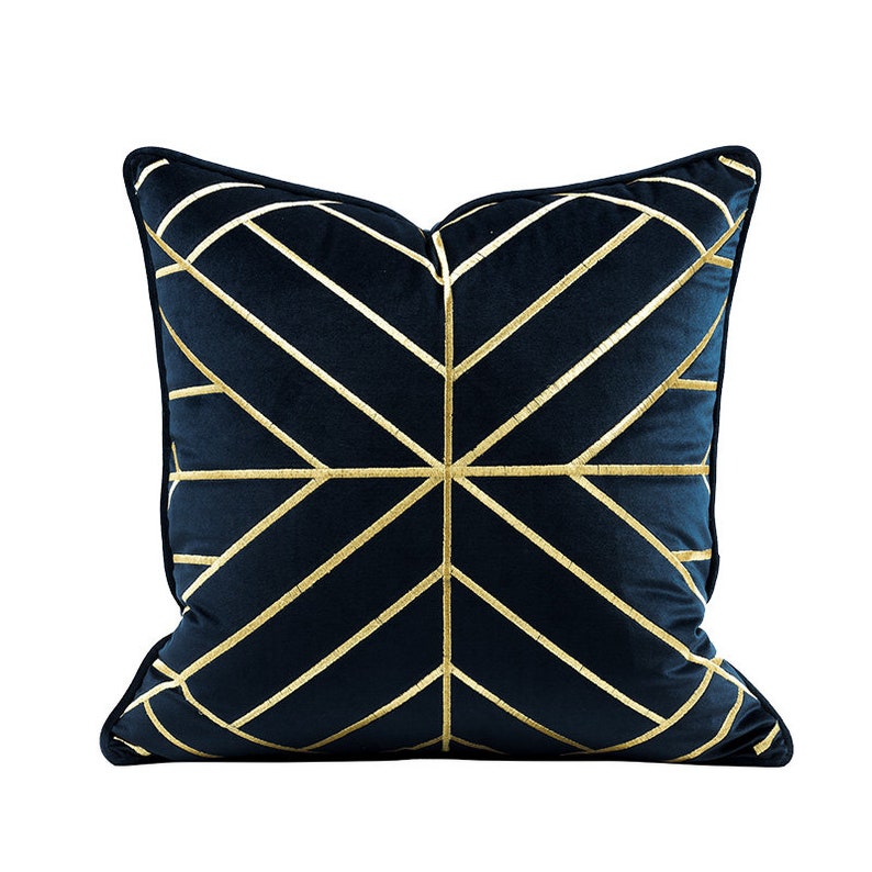 K&ouml;nnte beinhalten: Ein marineblaues Samtkissen mit einem geometrischen Muster aus goldener Stickerei.