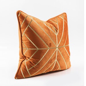 K&ouml;nnte beinhalten: Ein orangefarbenes Samtkissen mit einem geometrischen Muster aus goldener Stickerei.