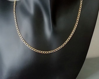 May include: A gold chain necklace on a black display stand. The chain is a curb style with a smooth finish.