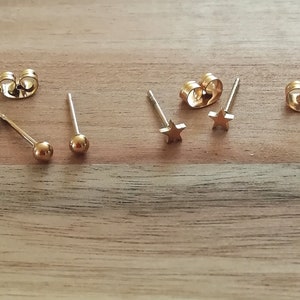 May include: A set of six gold-toned earrings. Two earrings feature a small ball at the end of the post, and four earrings feature a star-shaped charm.