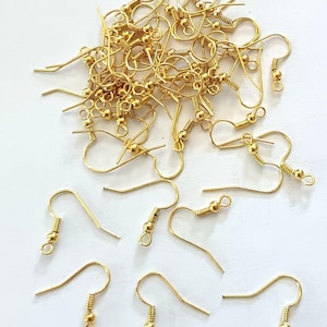 May include: A collection of gold-toned metal earring hooks, each featuring a curved wire, a small decorative coil, and a circular loop at the bottom for attaching jewelry components. The set includes a large pile of hooks and several individual pieces.