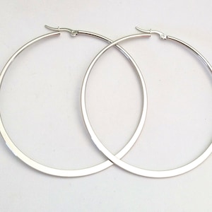 Peut inclure: Une paire de boucles d'oreilles créoles en argent avec un design plat et large. Les boucles d'oreilles sont simples et élégantes.