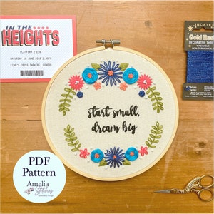 May include: Embroidered hoop art with a floral wreath and the text "start small, dream big". The hoop is on a wooden surface with a blue embroidery floss and a pair of gold scissors.