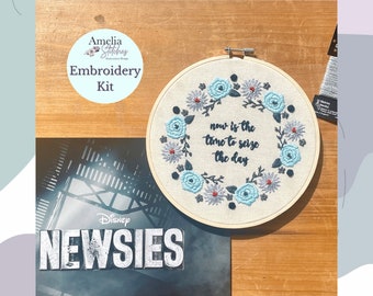 May include: An embroidery kit featuring a floral design with the text "now is the time to seize the day." The kit includes a wooden hoop, fabric, and thread. The kit also includes a "Disney Newsies" poster.