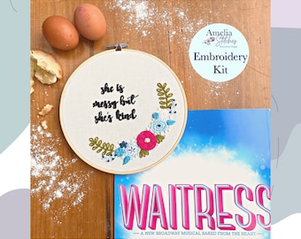 May include: An embroidery kit with the text "she is messy but she's kind" in a wooden hoop, surrounded by floral embroidery. The kit includes a "Waitress" musical playbill, eggs, and flour.