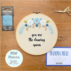 Pode incluir: Um aro de bordado branco com um desenho floral azul e branco e o texto "you are the dancing queen". Também está incluído fio de bordado azul, um bilhete para o musical Mamma Mia! e um padrão PDF.