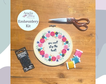 May include: Embroidery kit with a hoop featuring a floral wreath with the text "you can't stop the heat!" in black lettering. The kit includes embroidery floss, a needle, and a pair of scissors.