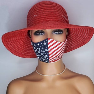 May include: A red wide-brimmed straw hat with a white and red striped face mask with pearl embellishments. The mask has a blue background.