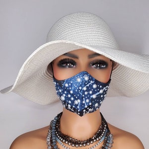 May include: A blue and white face mask with pearl embellishments. The mask is being worn by a mannequin with a white wide-brimmed hat and a layered necklace.
