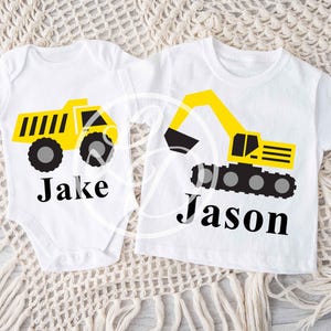 May include: Two white t-shirts with a yellow dump truck and excavator design. The shirts are personalized with the names "Jake" and "Jason".