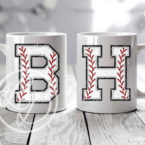 May include: Two white ceramic mugs with baseball-themed letter designs. The mug on the left has a red and white baseball stitch design with the letter "B" in the center. The mug on the right has a red and white baseball stitch design with the letter "H" in the center.