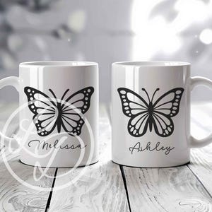 May include: Two white ceramic mugs with black butterfly designs and personalized names. The mug on the left says "Melissa" and the mug on the right says "Ashley".