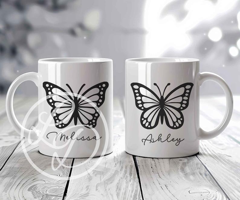 May include: Two white ceramic mugs with black butterfly designs and personalized names. The mug on the left says "Melissa" and the mug on the right says "Ashley".