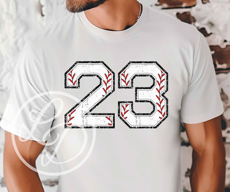 May include: White t-shirt with a distressed black and white number 23. The number is outlined in black and has a baseball stitch design in red.