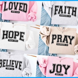 Puede incluir: Cinco sudaderas diferentes con varios mensajes religiosos impresos en ellas. Las sudaderas son de diferentes colores, incluyendo rosa, blanco, gris, beige y rosa claro. Los mensajes incluyen "Loved", "Faith", "Hope", "Pray" y "Joy". Cada mensaje est&aacute; impreso en letras negras con un contorno blanco. Las sudaderas son todas de estilo casual y ser&iacute;an perfectas para el uso diario.