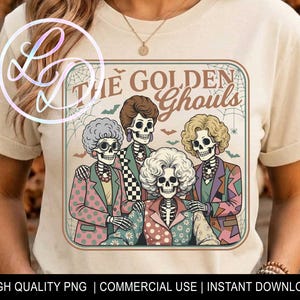May include: A cream-colored t-shirt featuring a graphic print of four skeleton figures with stylized hair and colorful patterned blazers. The text THE GOLDEN GHOULS is printed above the figures, surrounded by spiderwebs and small bat silhouettes.