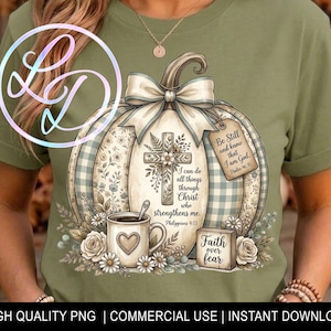May include: An olive green t-shirt featuring a graphic of a large pumpkin with a bow, a cross, a coffee mug with a heart, and floral accents. The text reads: I can do all things through Christ who strengthens me, Be Still and know that I am God, and Faith over fear.
