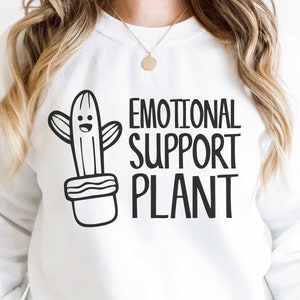 May include: White sweatshirt with a black and white illustration of a cactus in a pot and the text "Emotional Support Plant".