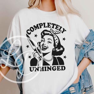 May include: White t-shirt featuring a black and white graphic of a vintage woman holding a knife, with the words "COMPLETELY UNHINGED" in a circular design. The design includes stars and a retro aesthetic.