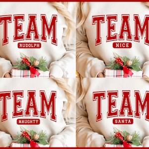 May include: Cream-colored sweatshirts with the word "TEAM" in red block letters. Each sweatshirt has a different word below "TEAM": "RUDOLPH", "NICE", "NAUGHTY", and "SANTA". The sweatshirts are paired with a wrapped gift and holiday greenery.