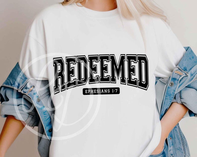May include: White sweatshirt with the word "REDEEMED" in bold, black, block letters. Below the word is the text "EPHESIANS 1:7" in a smaller, black font. The sweatshirt is worn with a denim jacket.