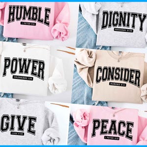May include: A collection of six crewneck sweatshirts in various colors, each displaying a different word in bold, black, and white collegiate lettering. The words include HUMBLE, DIGNITY, POWER, CONSIDER, GIVE, and PEACE, each with a corresponding Bible verse.