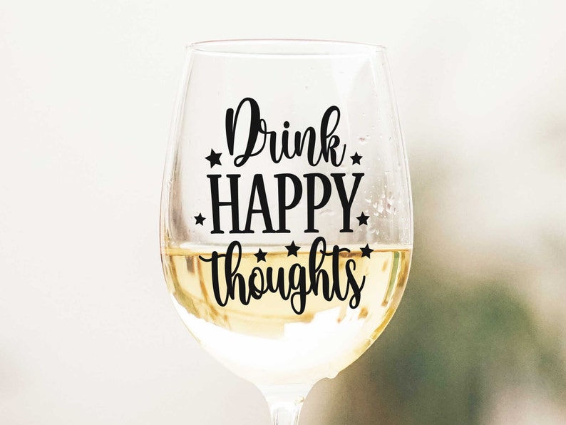 May include: A clear glass wine glass with a black vinyl decal that reads "Drink Happy Thoughts" with stars around the text.