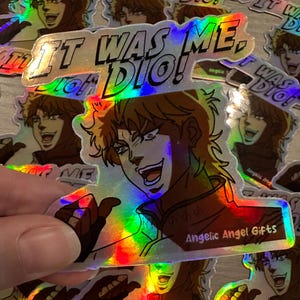 Könnte beinhalten: Holografischer Aufkleber mit einem Anime-Charakter und dem Text "IT WAS ME, DIO!". Der Charakter hat stachelige blonde Haare und ein rotes Outfit. Der Aufkleber hat einen Regenbogeneffekt. Der Text "Angelic Angel Gifts" ist unten aufgedruckt.