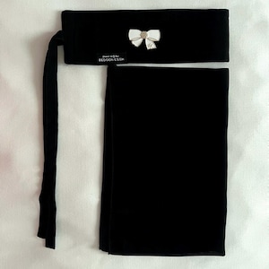 May include: Black headscarf set. The set includes a rectangular head covering and a matching band with a white bow and gold accents. The band also has text that reads "BEDOON ESSM".
