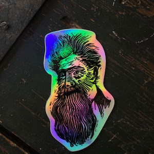 May include: A holographic sticker featuring a black and white illustration of a man with a long beard and a mustache. The man's hair is styled in a pompadour.