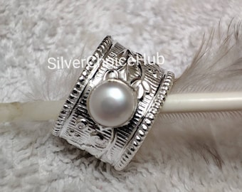 May include: Silver ring with a white pearl set in a floral design. The ring is made of silver and has a textured finish.