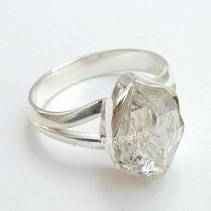 May include: A silver ring featuring a clear, faceted, diamond-shaped gemstone. The ring has a split band design.