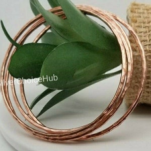 May include: Set of four hammered copper bangles. The bangles are stacked on top of each other and are a warm copper color.