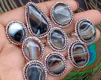 May include: A collection of silver rings with oval and teardrop-shaped black and white striped agate stones. Each ring has a twisted rope-like border. The rings are displayed on a hand, showcasing the variety of designs and stone patterns.