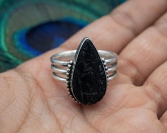 May include: A silver ring featuring a teardrop-shaped black stone set in a bezel. The band consists of three parallel silver wires that converge at the sides, with small decorative silver beads lining the edge of the stone setting.