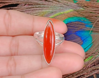 May include: A silver ring featuring a smooth, elongated marquise-shaped orange stone set vertically in the center. The band is composed of two thin silver wires that split and reconnect on each side of the central gemstone setting.