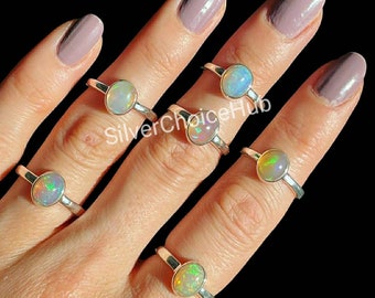 May include: Five silver rings with opal gemstones. The rings are on a hand with light pink nail polish.