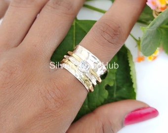 May include: A silver and gold spinning ring with a clear gemstone. The ring is worn on a finger.