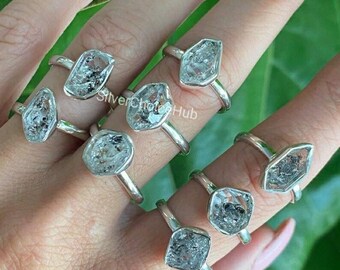 May include: A set of silver rings featuring clear, faceted, geometric quartz stones. The rings are stacked on a hand, showcasing the unique shapes and sparkle of the stones.