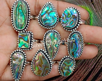 May include: A set of nine silver rings with abalone shell inlays. The rings feature different shapes, including oval, teardrop, and square. The abalone shell has a beautiful iridescent sheen with shades of green, blue, and purple.