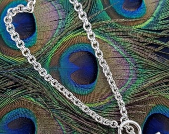 May include: A silver-toned chain necklace featuring a series of uniform circular links connected in a continuous loop. The necklace is secured with a toggle clasp consisting of a circular ring and a straight metal bar that passes through the ring.