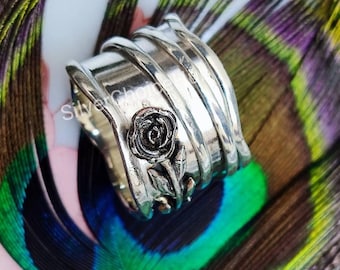 May include: A silver ring with a textured, hammered finish and a rose design. The ring is wide and has a unique, organic shape.