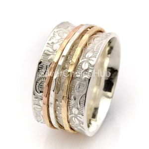 May include: A silver spinning ring with three bands of rose gold. The ring is decorated with a floral pattern.