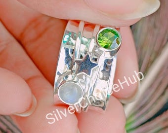 May include: A silver spinning ring with a green gemstone, a white moonstone, and a star charm. The ring is on a finger.