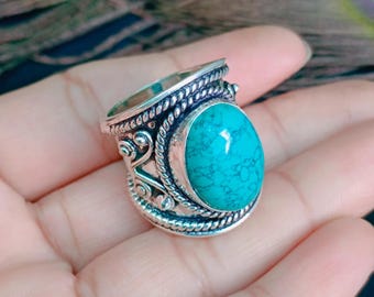 May include: A silver ring featuring a large, oval-shaped turquoise stone with dark veining. The band is crafted with intricate twisted rope detailing and decorative scrollwork patterns surrounding the central gemstone setting.