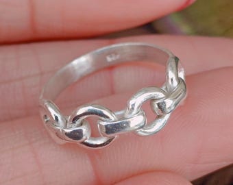 May include: A silver ring with a chain link design. The ring is made of a shiny, metallic material and features a series of interconnected links. The links are rounded and smooth, creating a continuous loop around the finger. The ring is a simple yet elegant piece of jewelry.