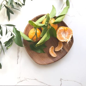 May include: A wooden bowl filled with whole and segmented mandarin oranges, with green leaves scattered around the bowl.