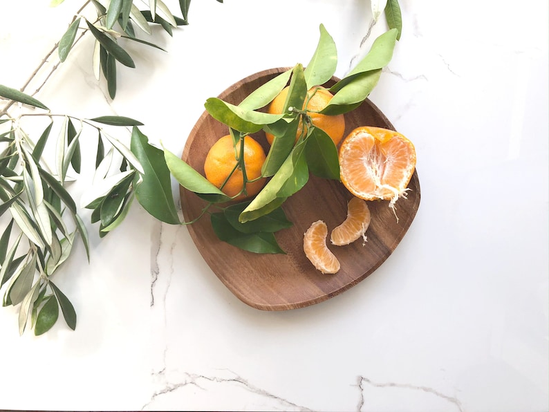 May include: A wooden bowl filled with whole and segmented mandarin oranges, with green leaves scattered around the bowl.